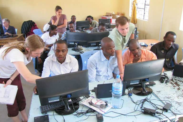 MSU students assisting Tanzania students on computers in classroom.