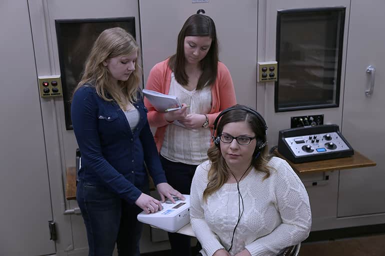 Two female undergraduate students performing a hearing test on another student.