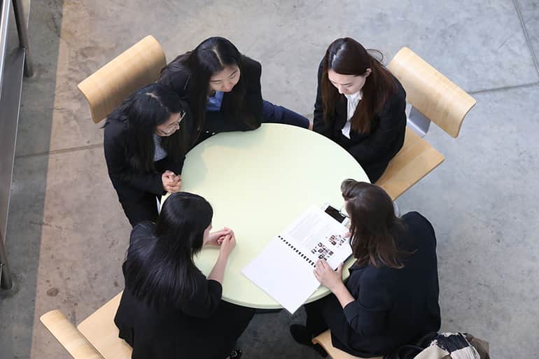Four female students sitting at a round table working with client on a presentation.