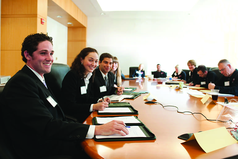 A group of sales leadership students sitting at a long conference table working with local clients.