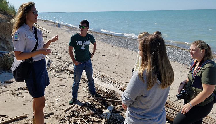 Michelle Polley, a naturalist at Pinery Park in Ontario, discusses skinks, toad balloons, marram grass, hognose snakes and karner blue butterflies with Knight Center students on a Lake Huron beach. The students traveled to Canada to study transboundary issues. From left Remington Sawege, Kaley Fech, Whitney McDonald, Quinn Zimmerman, Alexandria Iacobelli and Anntaninna Biondi. 