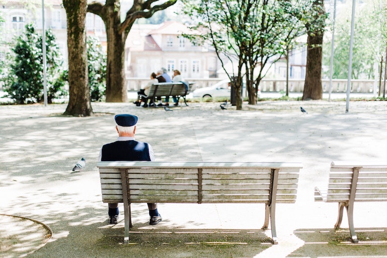 Photo of an elderly man sitting on a bench watching people in the park