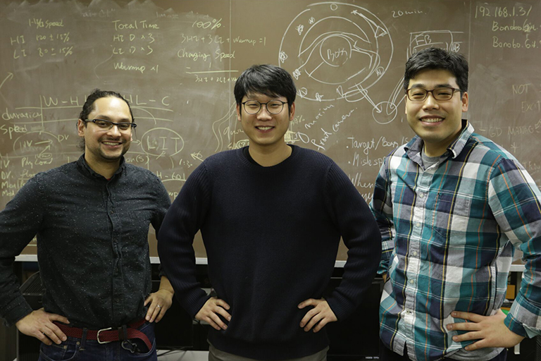 Ratan, Lee and Park stand smiling in front of a chalk board
