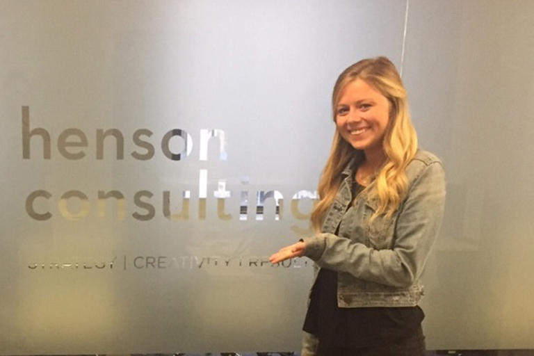 Alexandra DeVilling posing in front of the Henson Consulting sign.
