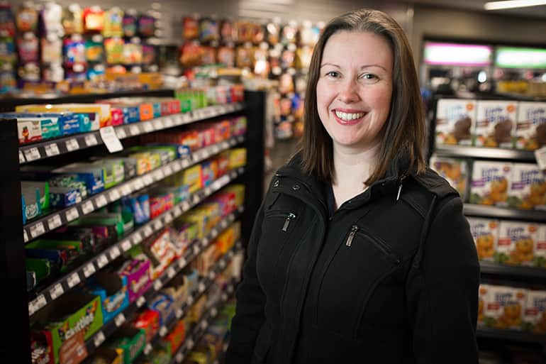 Professor Anna McAlister smiling as she stands next to snack items in grocery store.