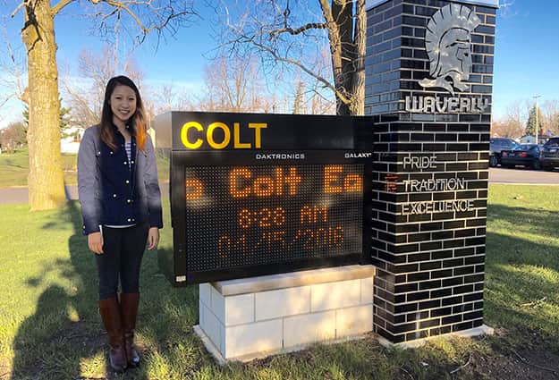 Joni Choi standing outside next to the Colt School sign.