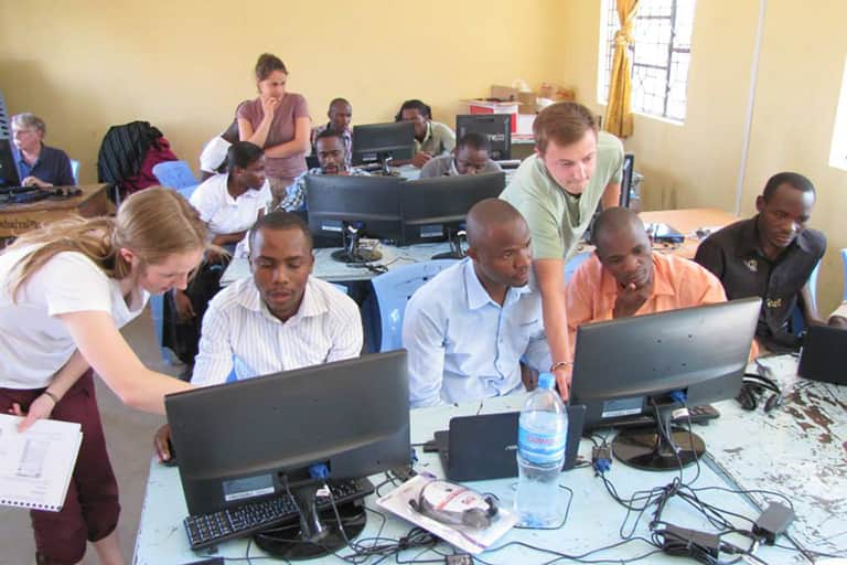Information and Communication Technologies for Development study abroad students assisting students in the class room on using computer equipment.