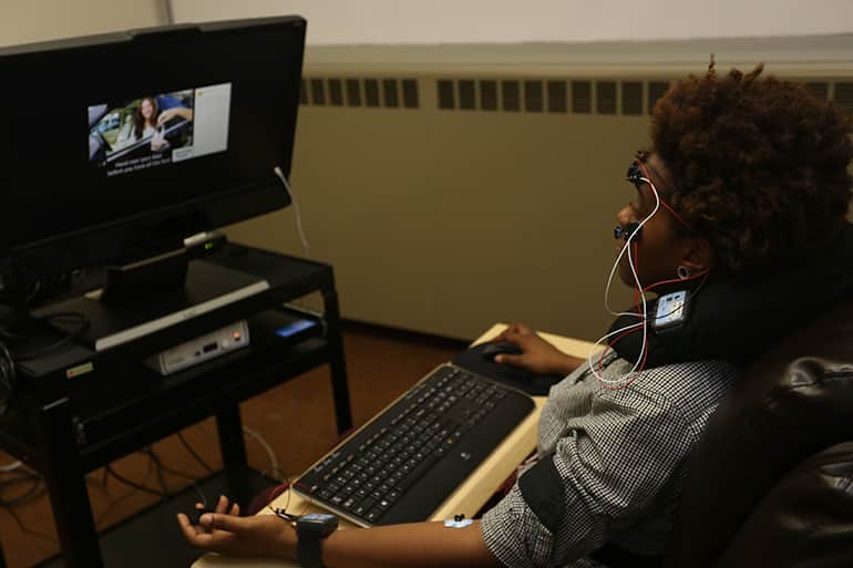 Female subject taking part in MAP lab experiement. She has electronic sensors attached to her head and hands and is watching advertisments.