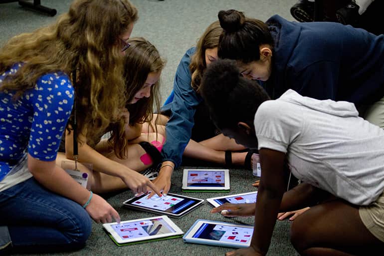 Five girls from the MSU Media Summer Camp are sitting on the floor designing games on iPads.