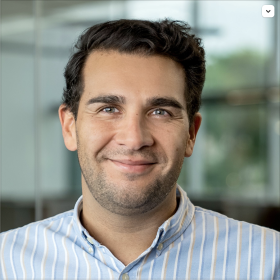 Dr. Juan Mundel looks at the camera over a blurry window background