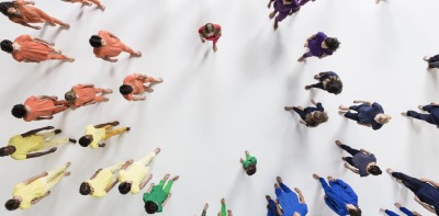 group of people standing in a spread out circle and dressed in a rainbow of colors