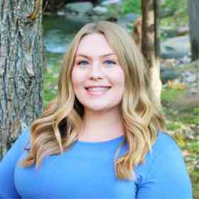 Kelsey is smiling while standing in front of trees.