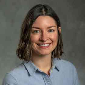 A headshot of Victoria Diedrichs, a white woman with chin-length, dark brown, wavy hair, wearing a light blue collared shirt.