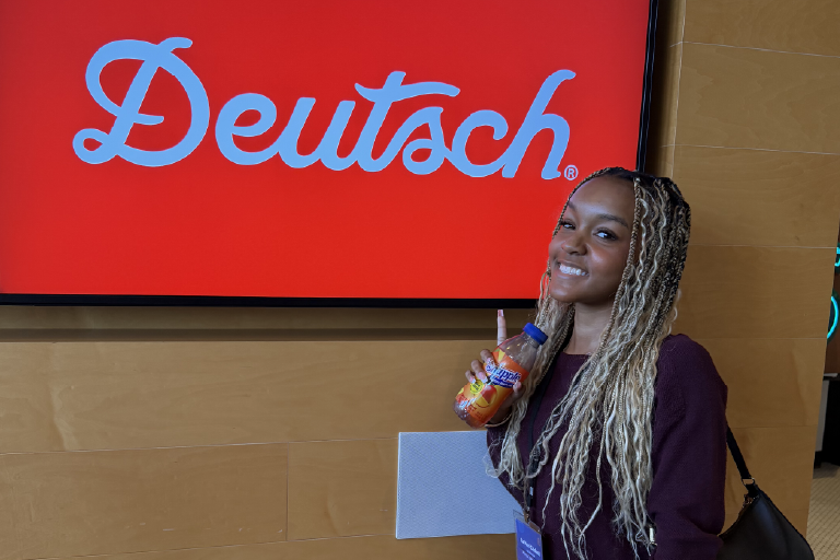 Ra’Moni Caldwell standing in front of the Deutsch sign