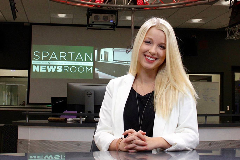 Journalism student sitting in the Spartan Newsroom smiling at the camera.
