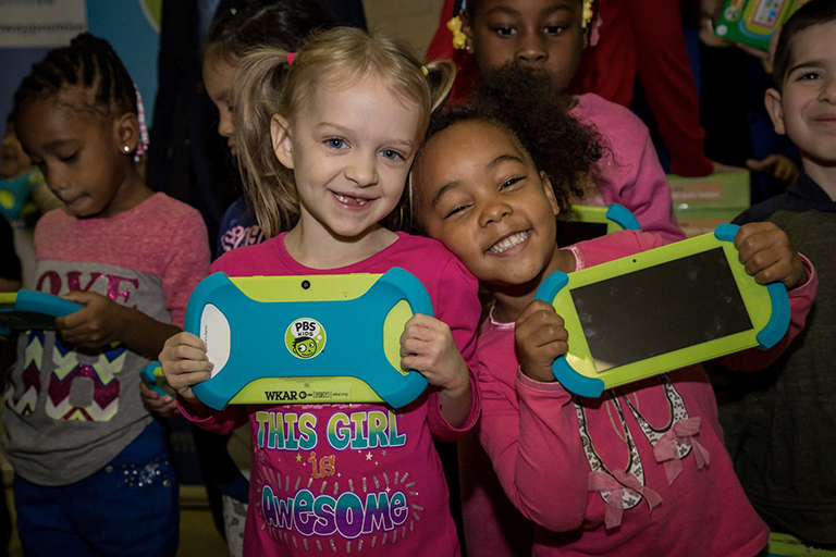 Two kindergarten girls holding their new playpads and smiling for the camera.