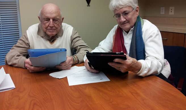 Elderly man and women sitting at a table learning how to use a tablet device.