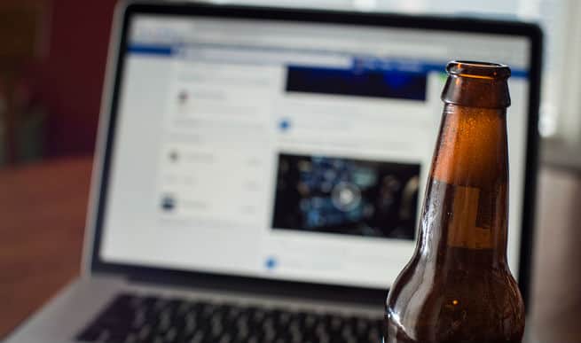 Beer bottle sitting in front of open laptop.
