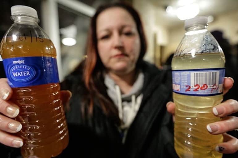 Woman from flint holding two bottles of water filled with dirty water that came from the tap.