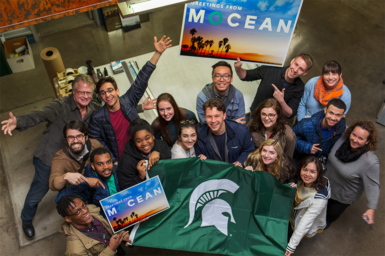 Top-town view of Craig Murray and interns holding signs, which read "Greetings from MOCEAN"