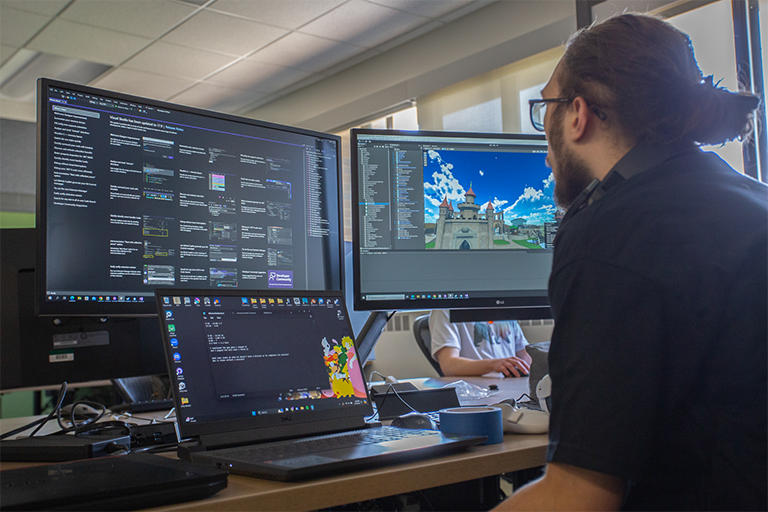 game design student works on a computer to build virtual world