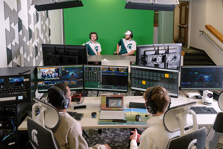 two MSU students run the esports broadcast stream while two more students comment on gameplay in front of a green screen.